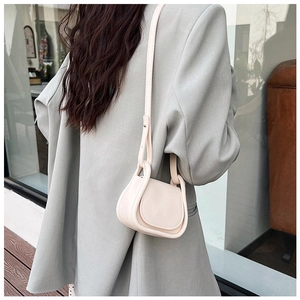 Mini borsa a sella color crema indossata su un blazer grigio stile moderno