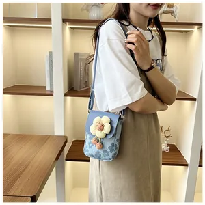 Détail d'un mini sac bleu à fleurs avec fleur 3D et pompon orange sur le rabat