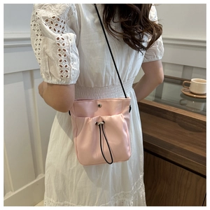 Pink satin drawstring bucket bag with black strap worn by model in minimalist setting