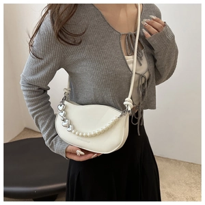 Detail of white pearl chain and heart pendant on a stylish semicircular shoulder bag