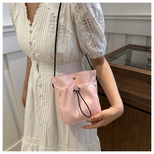 Detail van roze mini crossbodytas met trekkoord gedragen op een witte kanten jurk