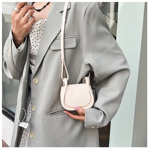 Mini borsa a sella crema indossata con blazer grigio per uno stile casual alla moda