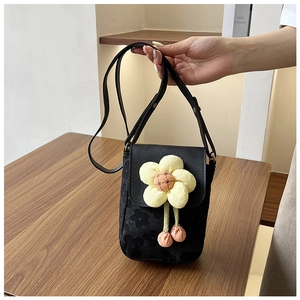 Détail du sac bandoulière noir avec fleur en peluche jaune posé sur une table en bois