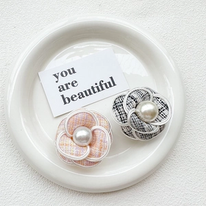 Close-up of camellia phone grips featuring tweed fabric and center pearl accents