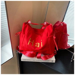 Close-up of red nylon tote bag with gold Hai embroidery on a decorative book