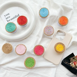 Colorful woven circular cell phone socket grips displayed on white fabric surface