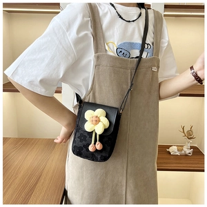 Détail d'un petit sac noir fleuri avec une fleur en peluche jaune et des pompons roses
