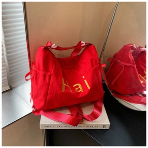 Detail of red canvas bag with golden Hai embroidery and side bows on an art book
