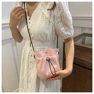 Detail van roze canvas crossbodytas met trekkoord gedragen op model met schouderriem