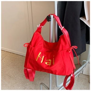 Macro detail of red nylon tote bag featuring yellow Hai embroidery and side bow detail