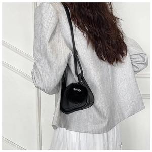 Détail d'un sac bandoulière noir avec pompon noir porté sur une veste grise chic
