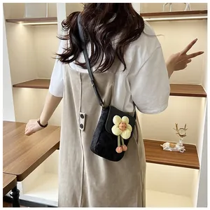 Mini sac à bandoulière noir avec breloque tournesol porté sur une robe beige clair