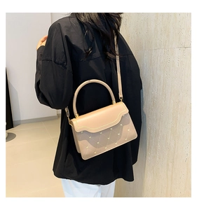 Detail of quilted texture with golden heart studs and scalloped flap on beige handbag