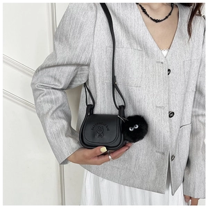 Détail du mini sac bandoulière noir avec lettrage embossé et pompon porté par un mannequin