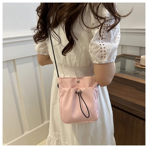 Rear view of a model wearing a pink drawstring nylon crossbody bag with metal buckle