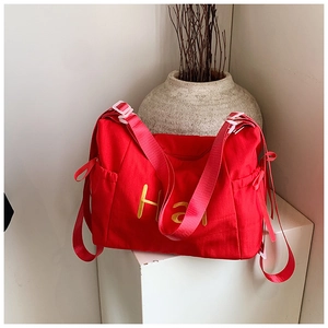 Detail of red canvas crossbody bag with yellow embroidered lettering and drawstring side pocket