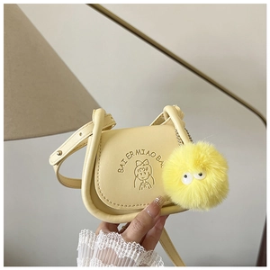 Détail d'un mini sac selle jaune avec relief de fille de dessin animé et pompon peluche