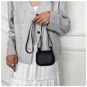 Dettaglio di una mini borsa a tracolla in pelle nera con patta arrotondata su una modella