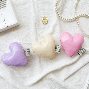 Detailed view of heart-shaped leather phone grips in purple, beige and pink on white fabric