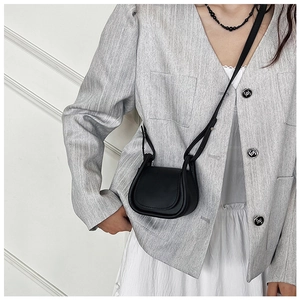 Dettaglio mini borsa a sella in pelle nera indossata con blazer grigio e gonna a pieghe bianca