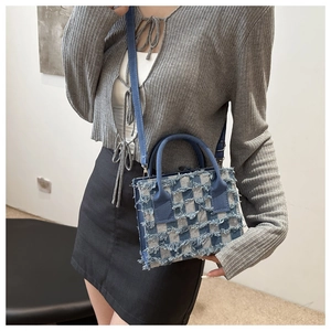Detail der blau-beigen karierten Jeans-Handtasche mit ausgefransten Blumenkanten und Gurt