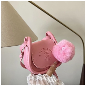 Détail d'un sac bandoulière rose avec logo cartoon embossé et pompon en peluche assorti