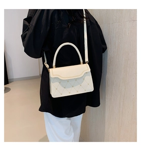 Detail of beige quilted handbag with golden heart accent and braided edge on flap