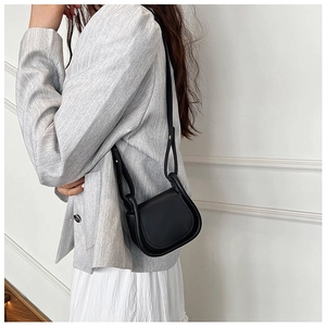 Mini borsa a tracolla in pelle nera indossata da una modella con tailleur grigio elegante