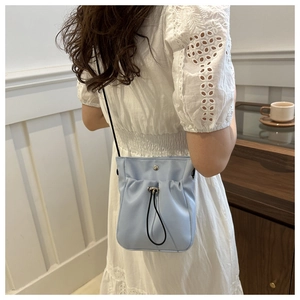 Detail view of light blue drawstring crossbody bag with pleated texture and silver snap