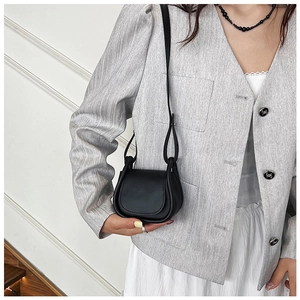 Mini borsa a tracolla in pelle nera indossata da una modella su un blazer grigio