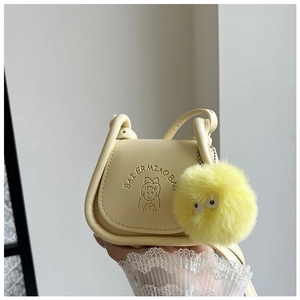 Gros plan d'un sac selle jaune crème avec imprimé dessin animé et pompon en fourrure jaune