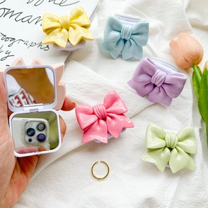 3D bow-shaped mirror phone grip in pastel macaron colors on a minimalist white fabric background