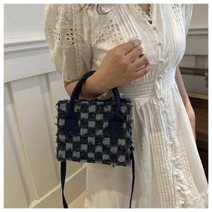 Makroansicht der ausgefransten Denim-Kanten und Karostruktur der Schachbrett-Handtasche