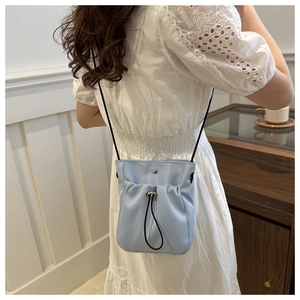 Detail of light blue drawstring crossbody bag worn by a model in a minimalist room