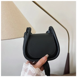 Dettaglio di una borsa a sella nera minimalista tenuta su un polsino in pizzo bianco