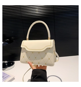 Detailed shot of cream quilted handbag featuring gold heart charms and woven trim edges
