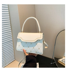 Detail of white heart-quilted crossbody bag with gold hardware and curved flap