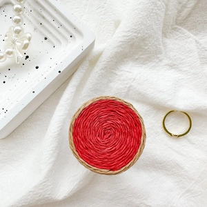 Detailed top view of red woven phone grip with textured straw border on white fabric