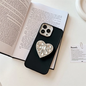 Détail de la coque iPhone noire mate avec support cœur en strass étincelants sur un livre
