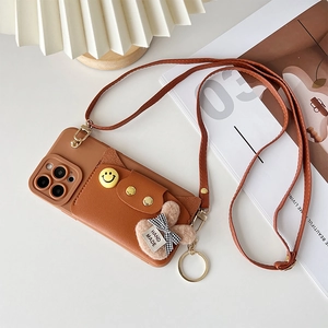 Close-up of brown leather iPhone case with smiley wallet, crossbody strap, and bunny charm