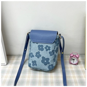 Détail d'un petit sac de téléphone floral bleu avec rabat uni sur une nappe à carreaux