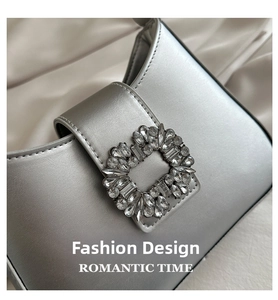 Close-up of silver PU leather handbag with oversized rhinestone buckle on satin background