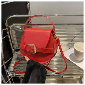 Detail of red leather crossbody bag featuring a large gold buckle and a handle