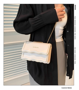 Detail of cream crossbody bag featuring a unique layered wave flap and golden chain strap
