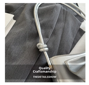 Detailed close-up of knotted shoulder strap on a silver metallic textured handbag