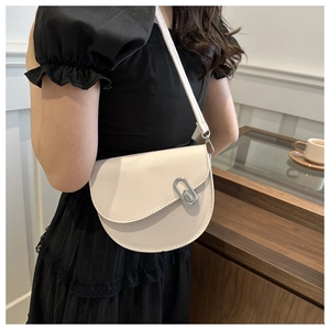 Detail of a creamy white saddle bag featuring a silver oval twist lock and slim strap