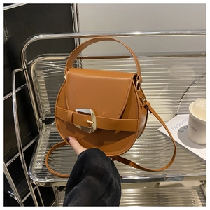 Detail of caramel brown saddle bag with gold buckle on a transparent chair with lifestyle props