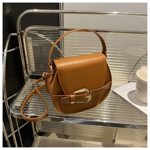 Detail of caramel leather half-moon bag featuring large gold buckle and shoulder strap