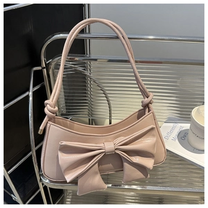 Close-up of light pink glossy bow underarm bag with elegant knot strap and gold hardware