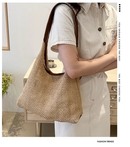 Detail of woven straw tote bag with brown leather handles worn by a model in a cozy room